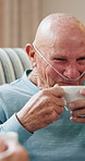 Coffee, relax and senior man on sofa in home with talking, gossip or conversation in living room. Happy, sick and elderly male person drinking warm beverage with discussion in lounge at house.