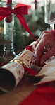 Person, hands and christmas cracker with decor for dining, festive preparation or design in home. Crockery, decorations or table setter with red ribbon for december celebration or holiday tradition
