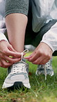 Hands, running shoes and tie with laces on grass for fitness, ready and feet for wellness at urban park. Person, runner and outdoor with sneakers, legs or start on ground with exercise in nature