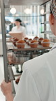 Woman, pastry chef and trolley with muffins in bakery for catering service, hospitality or serving. Female person, culinary artist or pushing cart with rack of baked goods for dessert in kitchen