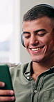 Headphones, smartphone and man in home, smile and listening to music, internet and relax. Apartment, mobile user and person in lounge, cellphone and streaming for radio, audio and app for podcast