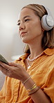 Woman, phone and happy with headphones in home for streaming, relax and dance in living room. Person, smile and smartphone for audio subscription, mobile app or listen to music on couch at apartment