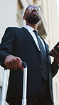 Waiting, phone and businessman in city with luggage for transport, lift service and taxi. Low angle, lawyer and African person with suitcase on cellphone for travel, commute and order cab in town