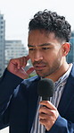 Businessman, reporter and listening with mic in city for announcement or breaking news. Business, anchorman or journalist with important alert signal for public broadcast, commercial or radio report