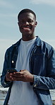 Ocean, face and black man with phone, internet for online chatting and tourism for summer holiday. Happy, mobile user and person with tech for social media, vacation and connection for message