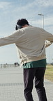 Happy man, music and dancing with headphones on beach promenade for audio streaming or playlist. Back view, excited or male person jumping in air with sound app, energy or vibe for outdoor freedom