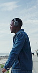 Happy man, online and headphones for music at beach, relax and listening to entertainment on weekend. Ocean, tourist and person with technology for audio, calm and streaming song on holiday break