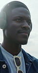 Headphones, outdoor and black man by beach for vacation with listening to music, playlist or radio. Relax, audio tech and person on promenade by ocean for streaming album on holiday or weekend trip.