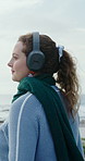Happy woman, online and headphones for music at beach, relax and listen to entertainment on weekend. Outdoor, tourist and person with technology for audio, smile and streaming song on winter holiday