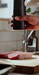 Kitchen, steak and hands of chef with pepper for cuisine, dinner and gourmet recipe for lunch. Cooking, food and person with meat, protein and seasoning for meal prep, nutrition and culinary skills