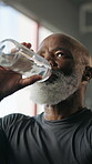 Fitness, drinking water or old man in gym with break, workout fatigue or hydration in intense practice. H2o, rest or senior person with bottle, training pause and recovery for performance goals.