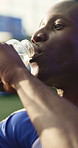 Soccer, man and drinking water with training break for practice, fitness or hydration for recovery. Thirsty, black person or happy footballer outdoor with bottle, electrolytes or wellness for athlete