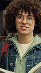 Education, face and happy man with book in library, learning and confident for academic development. College, glasses and person with smile for knowledge, student and exam preparation with textbook