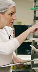 Woman, clipboard and count stock in bakery for inspection, manager or checklist at workplace. Mature person, industrial kitchen and writing on paper for quality assurance or cost of baking process
