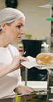 Woman, clipboard and check bread in bakery with inspection, manager or checklist at workplace. Mature person, industrial kitchen and writing on paper for safety and sanitation of baking process