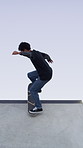 Man, ramp and stunt with skateboard for exercise, extreme sports and practice with streetwear. Skateboarder, training and low angle at skatepark for challenge, hobby and balance outdoor with blue sky