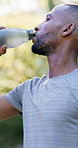 Fitness, drinking and black man with water in nature for hydration, electrolytes and bottle for exercise. Sports, outdoor and person with liquid for wellness, health and thirsty for active hobby