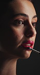 Brush, makeup and lipstick with woman in dark studio for application of cosmetics product. Beauty, makeover and tool with person on black background to apply red lip gloss to mouth for glow or shine