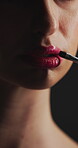 Brush, mouth and lipstick with woman in dark studio for application of cosmetics product. Beauty, makeup and tool with person on black background to apply red lip gloss for glow, makeover or shine