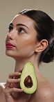 Thinking, woman and skincare with avocado for beauty, vitamin c and brighten skin in studio background. Vision, person and fruit for organic cosmetics, facial hydration and antioxidants for self care