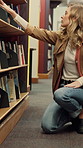 Woman, student and library with bookshelf for education, learning or information in university. Female person, academic or learner looking in aisle with books for story, novels or study material