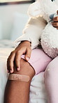 Hands, kid and sad face with knee bandage on bed for bruise, medical injury or fall in home visit. Healthcare, support and child with first aid plaster for nursing, accident or wound protection