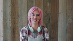 Face, woman and punk fashion with smile, headphones and pink hair for edgy aesthetic by wood background. Happy, person and alternative style with audio tech, tattoo and piercings for individuality.