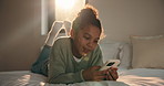 Girl, typing and bed with phone for social media, communication or connection in home. Child, kid or teenager relaxing with smile, lens flare or mobile smartphone in bedroom for online chatting app