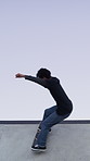 Man, ramp and stunt with skateboard for fitness, extreme sports and practice with streetwear. Skateboarder, training and low angle at skatepark for challenge, hobby and balance outdoor with blue sky