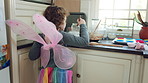 Child, butterfly wings and baking in kitchen, development and learn culinary skills with ingredients. Kid, growth and girl with creative costume, cooking and dessert preparation with recipe in house