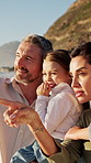 Happy, parents and children at beach with summer holiday, point and bonding together for family trip. People, mother smile and father outdoor by ocean with girl kids, travel vacation and discussion.