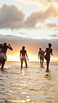 Sunset, walking and friends in ocean for holiday, tropical destination and summer break for adventure. Island vacation, travel and people with coastal trip for bonding, getaway or sunshine from back