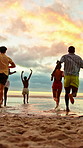 Running, friends and group at beach for holiday, travel or fun together in nature on weekend getaway. Outdoor, sunset and freedom on summer vacation, back and bonding with people on sea adventure
