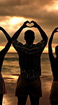 People, night and beach with heart hands for love, outdoor romance or care together in nature. Back view, community or group of friends with shape or romantic gesture in late evening on ocean coast
