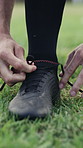 Person, hands and tying shoes for sport preparation, exercise or outdoor training on grass field. Active, athlete or rugby player getting ready with laces or boots for fitness, match or game on pitch