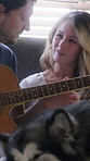 Love, couple and guitar in home with dog, conversation and bonding together on weekend break. Pet, man and woman with acoustic instrument to play music, talking and connection with husky in house
