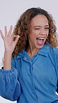 Woman, face and wink with OK in studio for review, vote or excited opinion on white background. Hand sign, yes signal or emoji with happy female person, playful and like for support or approval