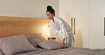 Woman, cleaning and bedroom at house with pillows, fresh linen and start day with chores. Person, wake up and neat bedding in home for housekeeping, cleanliness and tidy bed with comfortable fabric