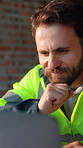 Construction, laptop and thinking with man on building site for planning or property development. Computer, reading and research with developer on worksite for architecture or project management