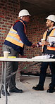 Construction, engineer and men shaking hands for greeting, welcome or collaboration for teamwork. Smile, architecture or handshake for partnership, plan or development with blueprint at building site