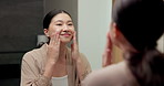 Mirror, skincare and asian woman with lotion in bathroom for grooming or moisturizer in home. Female person, face cream and applying beauty cosmetics with smile or reflection for dermatology in house