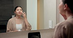 Mirror, skincare and asian woman with face cream in bathroom for grooming or moisturizer in home. Female person, lotion and applying beauty cosmetics with smile or reflection for dermatology in house