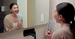 Singing, happy and Asian woman with brush in bathroom mirror for fun, grooming and morning routine. Reflection, home and person with song, karaoke and good mood for wellness, cleaning and self care