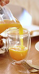 People, hands or pouring with orange juice on dining table for vitamin C drink or nutrition in home. Parent, child or beverage with natural organic citrus for healthy liquid, diet or blend in house