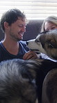 Playing, smile and couple with dogs in bedroom for bonding, animal companion and hug for connection. Support, embrace and happy people with security for wellness, stroke pets and laughing in home