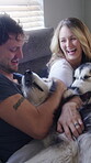 Hug, smile and couple with dogs in bedroom for bonding, animal companion and playing for connection. Support, embrace and happy people with security for wellness, stroke pets and laughing in home