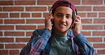Headphones, happy and face of student by brick wall for listening to music, playlist or radio at high school. Smile, audio tech and portrait of boy teenager with streaming album online at campus.