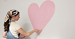 Woman, heart and pink with paint on wall for nursery, love or fun activity for home decor or style. Female person, painter or shape with romantic gesture, icon or symbol for mural art in house