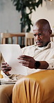 Finance, home or black man with documents on sofa for budget planning, expenses or mortgage bills. Male person, reading or checking financial invoice for insurance policy or asset management in house