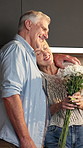 Flowers, happy and senior couple in kitchen for surprise, celebration and gift for love in home. Marriage, hug and man and woman with bouquet, smile and embrace for affection, trust and connection